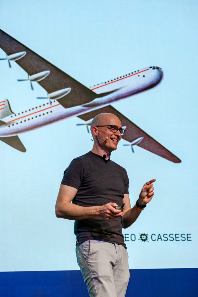 Matteo Cassese presenting with vintage airplane graphic slide on stage.